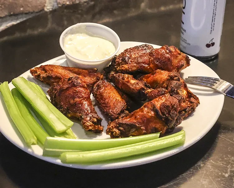 Plate of crispy chicken wings, celery sticks, and creamy dipping sauce.