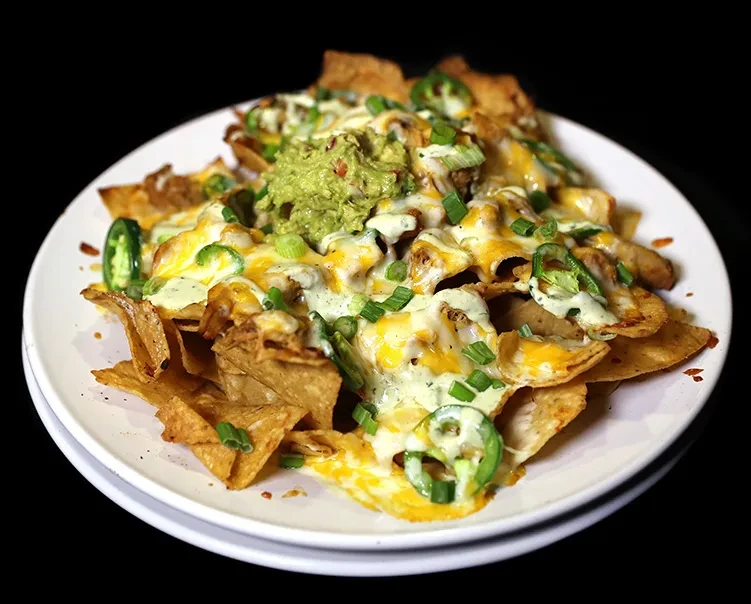 Nachos with melted cheese, guacamole, jalapeños, green onions, and white sauce.