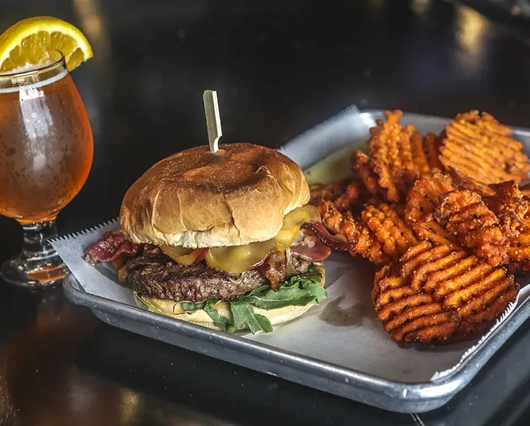 Gourmet burger with bacon, waffle-cut sweet potato fries, and amber beer.