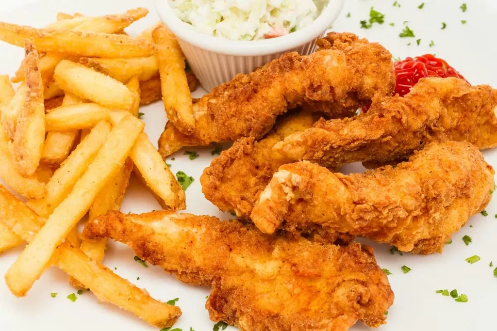 Fried chicken tenders, french fries, coleslaw, and ketchup on a white plate.