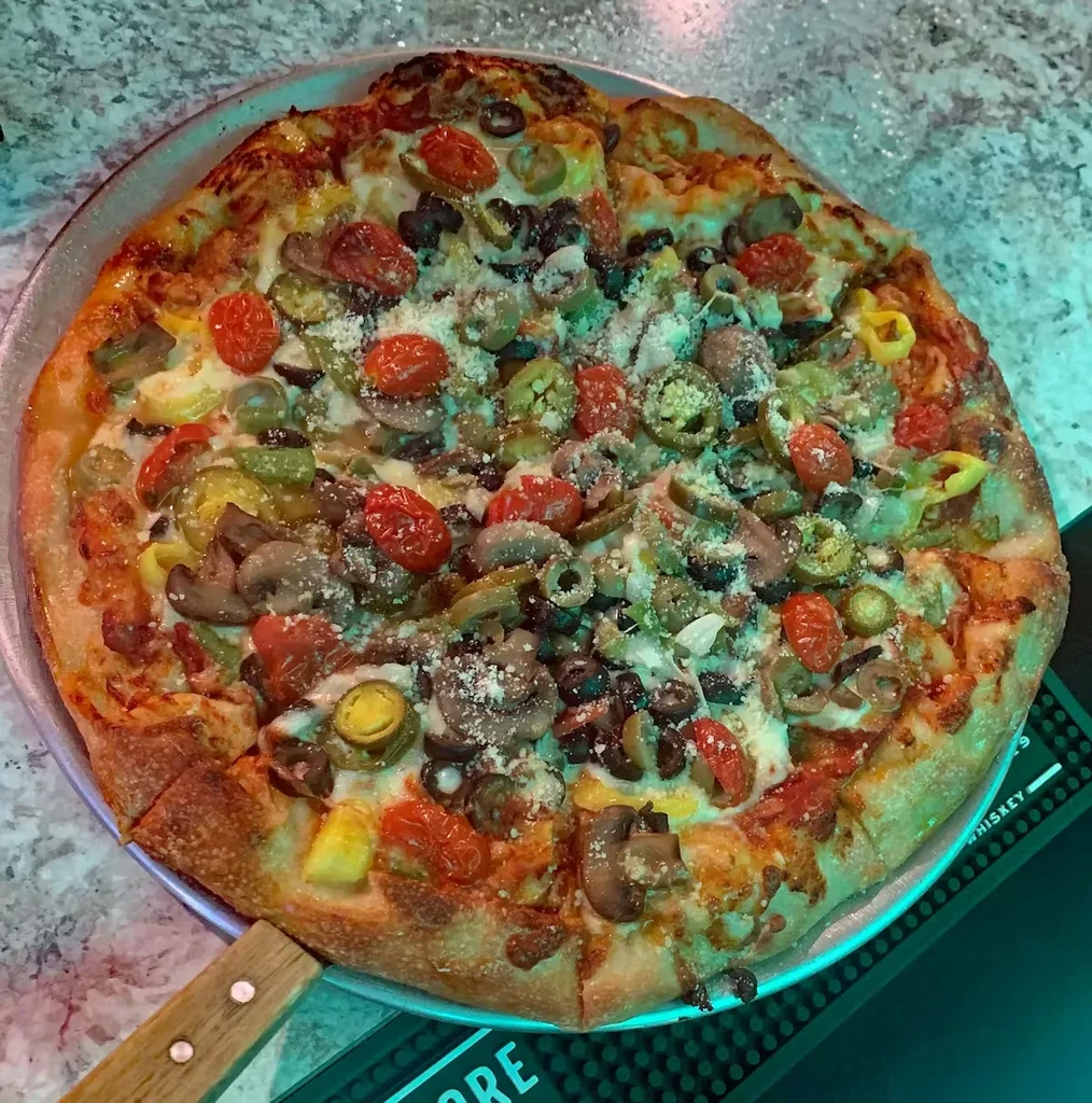 Round pizza with cheese, tomatoes, olives, mushrooms, peppers on a pan.