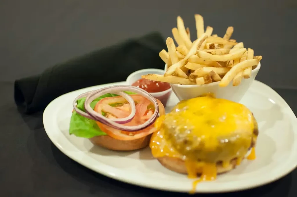 Cheeseburger with melted cheese, toppings, french fries, and ketchup.