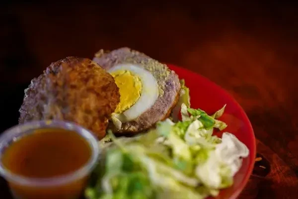 Halved Scotch egg with purple-tinted coating, green salad, and dipping sauce.