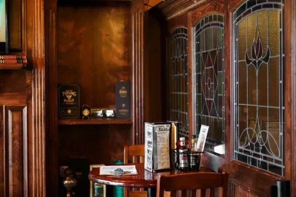 Cozy pub interior with dark wood, stained glass, and whiskey bottles.