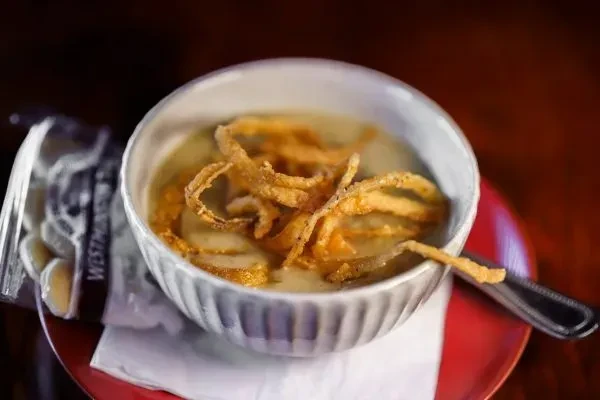 Close-up: Creamy soup with crispy fried onions, crackers on red plate.