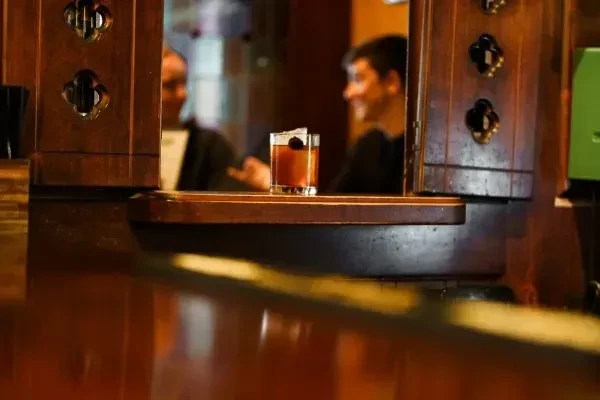 Amber cocktail with cherry and ice, blurred bar background.