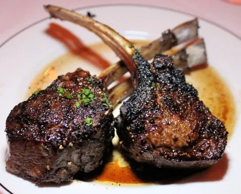 Two seared lamb chops with herbs and glossy sauce on a white plate.