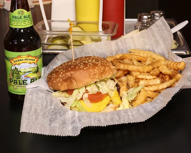 A cheeseburger, crinkle fries, and Sierra Nevada beer on a table.