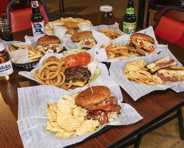 Table laden with burgers, fries, sandwiches, and bottled beers.
