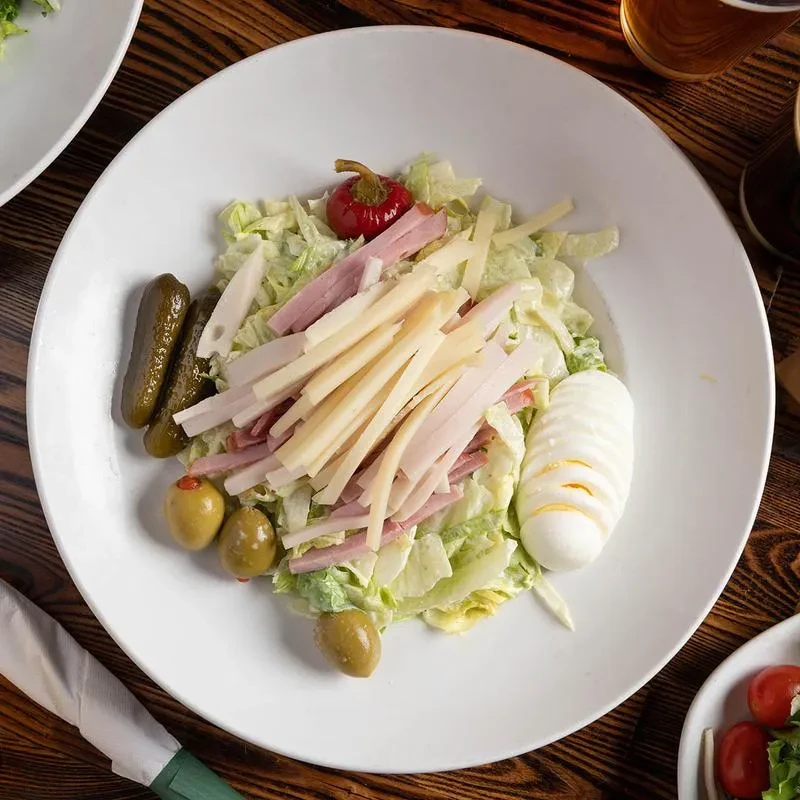 A large chef salad with ham, cheese, egg, olives, and pickles.