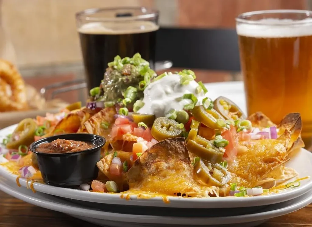 Loaded nachos with cheese, vegetables, sour cream, guacamole, salsa, and drinks.