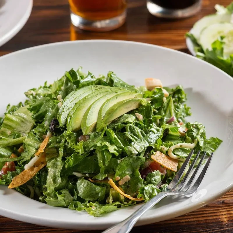 Green salad with fanned avocado, tortilla strips, and fork on white plate.
