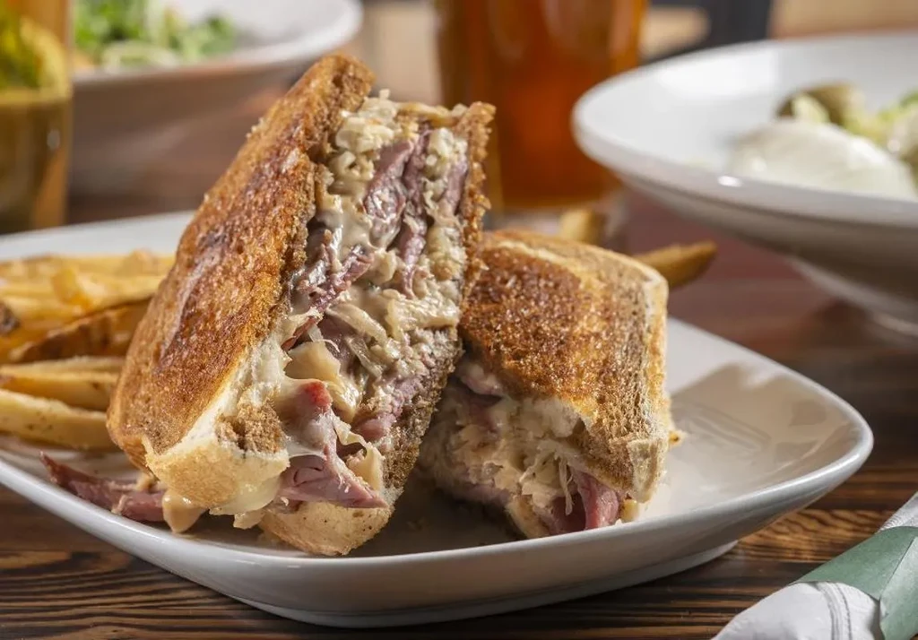 Toasted Reuben sandwich cut in half, with fries on a restaurant plate.