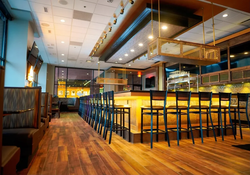Warmly lit modern restaurant interior with bar, stools, and booths.