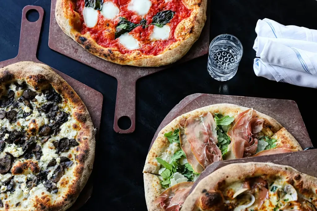 Four artisan pizzas: Margherita, mushroom, prosciutto, and another with seafood.
