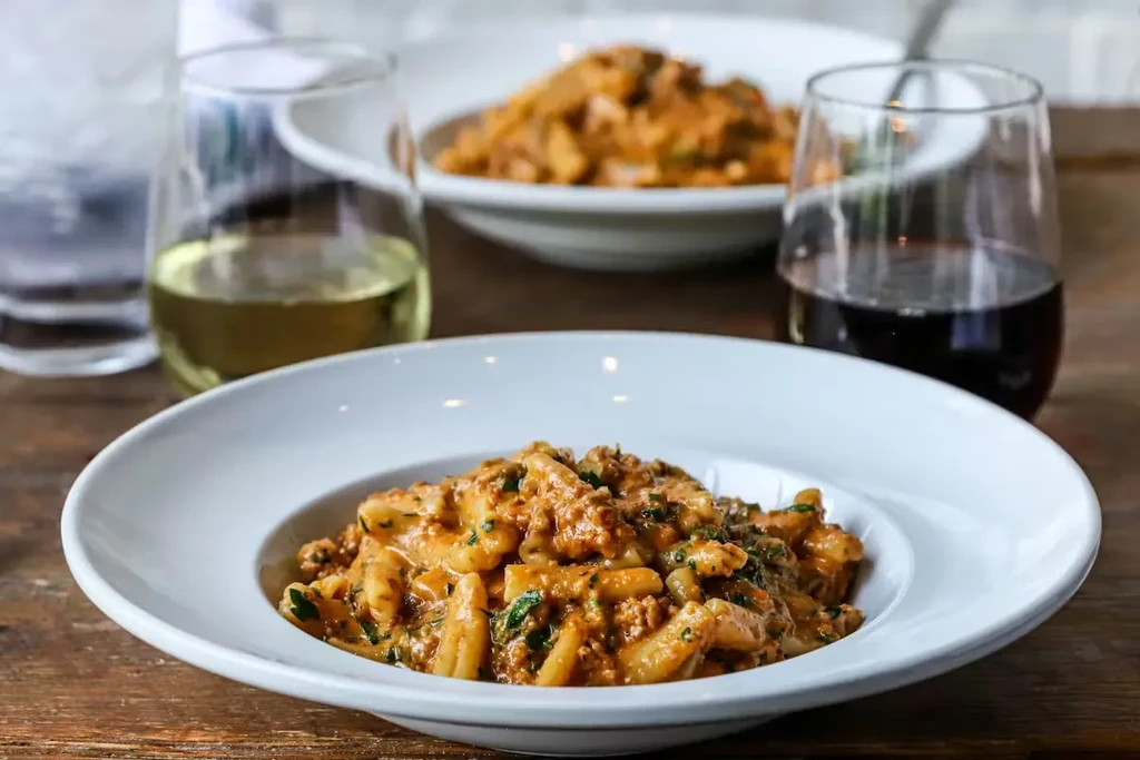 Pasta with meat sauce, white and red wines, water, on wood table.
