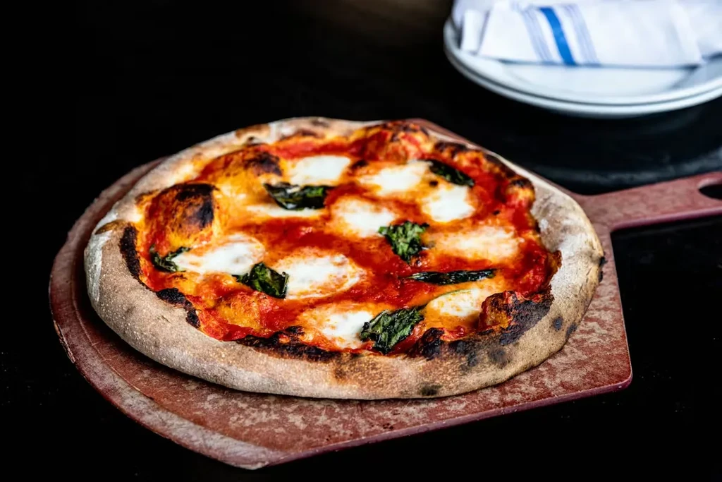 Margherita pizza with charred crust and basil on a rustic peel.