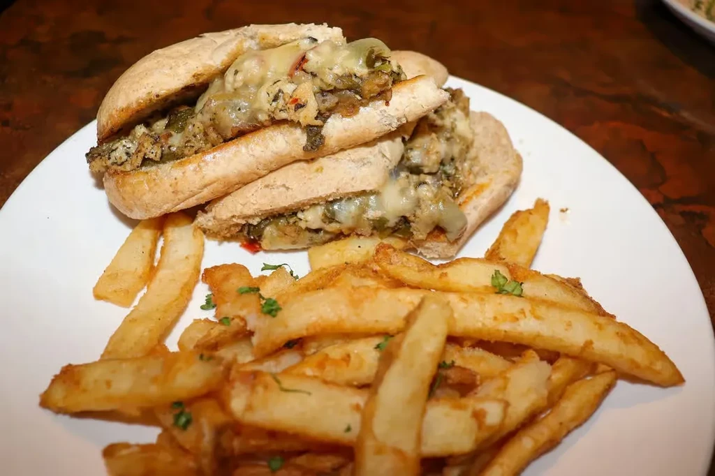 Melted cheese sub sandwich with green vegetables and french fries.