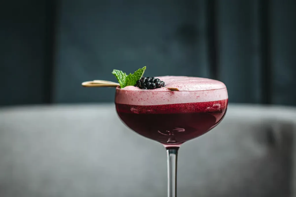 Two-layered cocktail in a stemmed coupe glass with blackberry and mint.