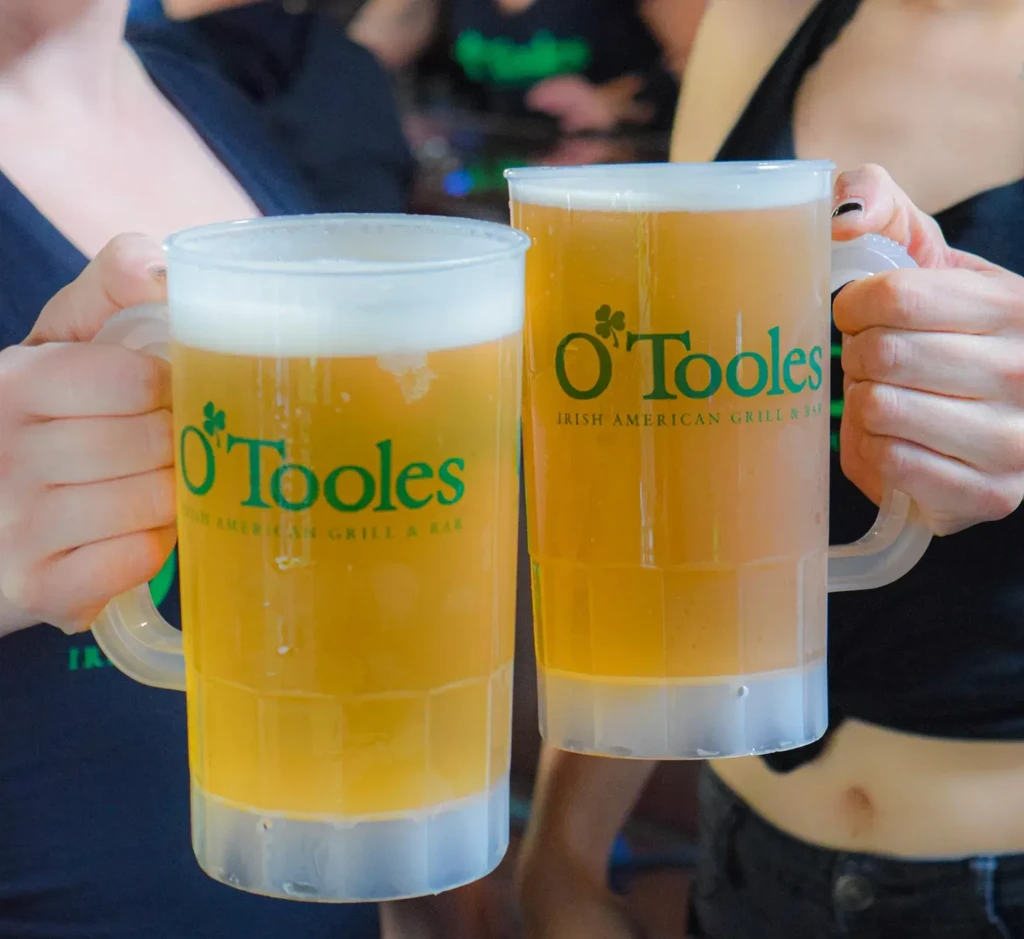 Two people toasting with O'Toole's branded beer mugs filled with foamy beer.