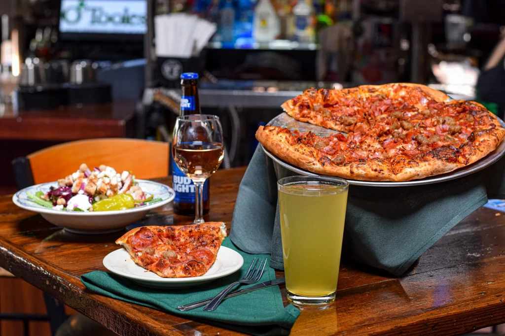 A restaurant table at O'Tooles with pizza, salad, and drinks.