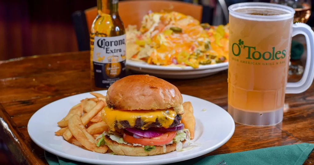 Cheeseburger, fries, nachos, O'Toole's beer, and Corona bottle on a wooden table.