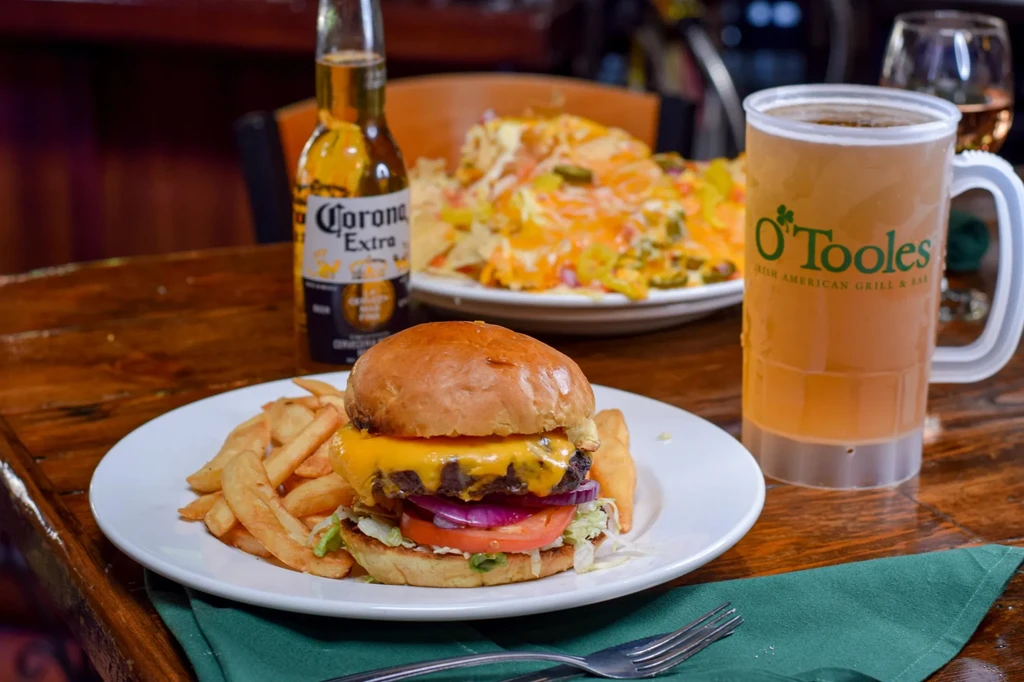Cheesy burger, fries, beers, and nachos on a rustic table.