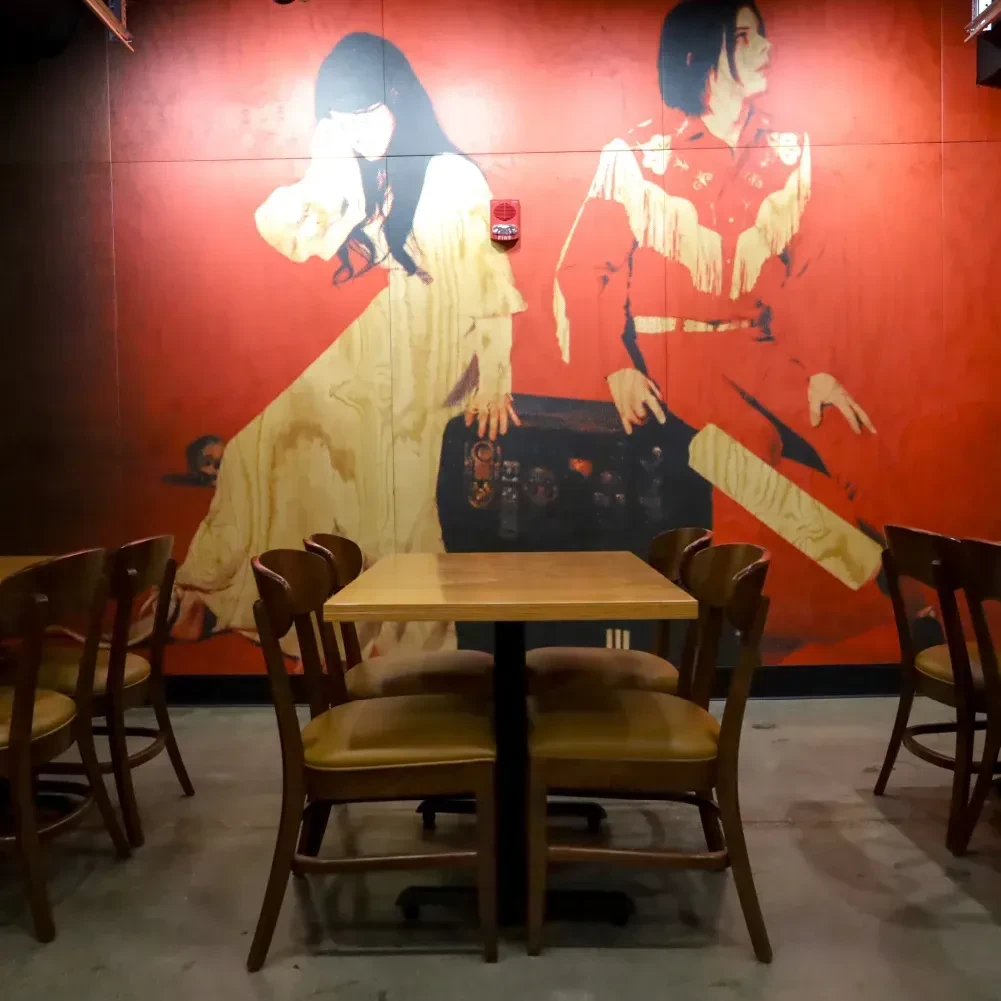 Red mural of two figures in empty restaurant with wooden tables.