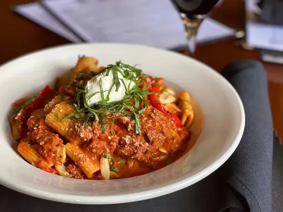 Rigatoni pasta with meat sauce, creamy ricotta, and fresh green herbs.