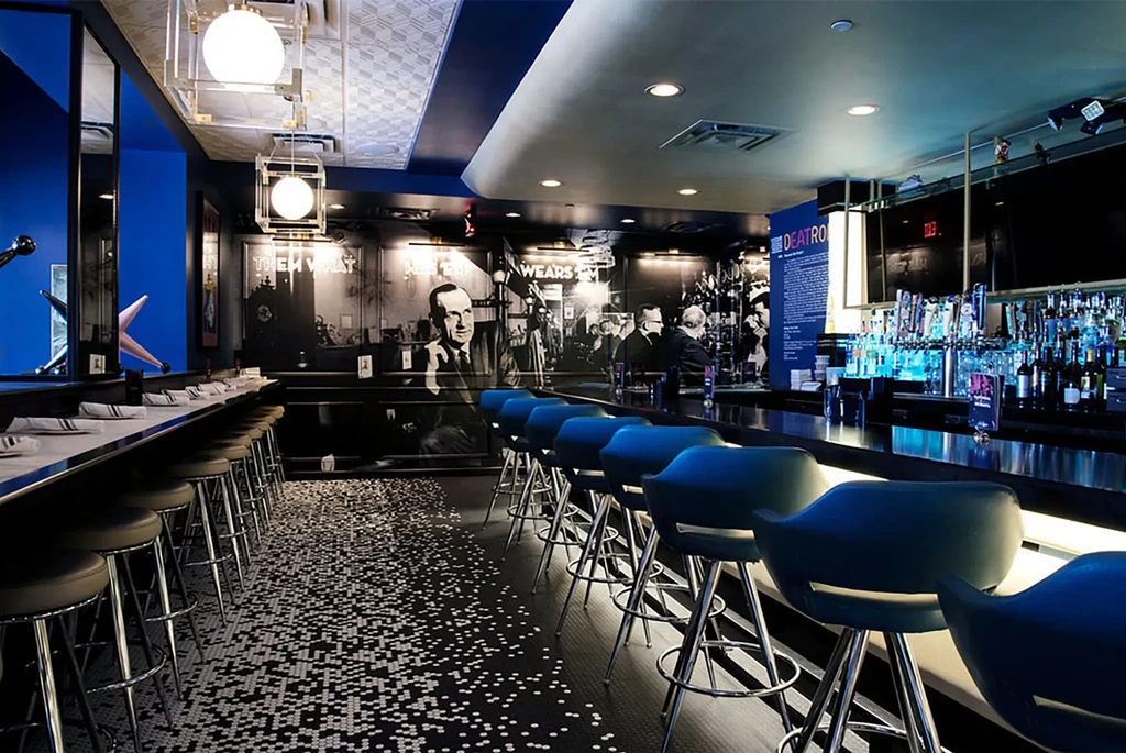 Modern restaurant bar with blue underlighting, mosaic floor, and portrait murals.