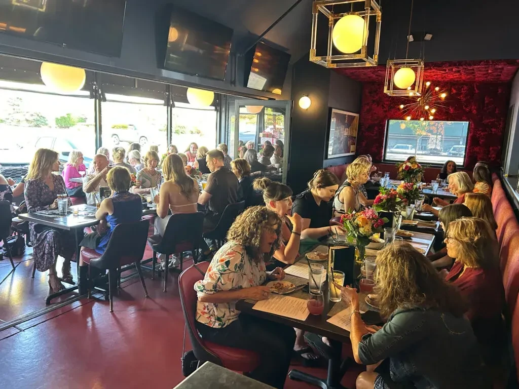Modern restaurant with dark walls, red velvet, and many social patrons.