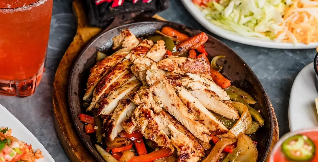 Sizzling grilled chicken fajitas with peppers and onions in a skillet.