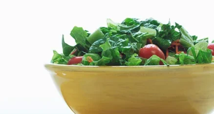 Vibrant green salad with cherry tomatoes and carrots in a yellow bowl.