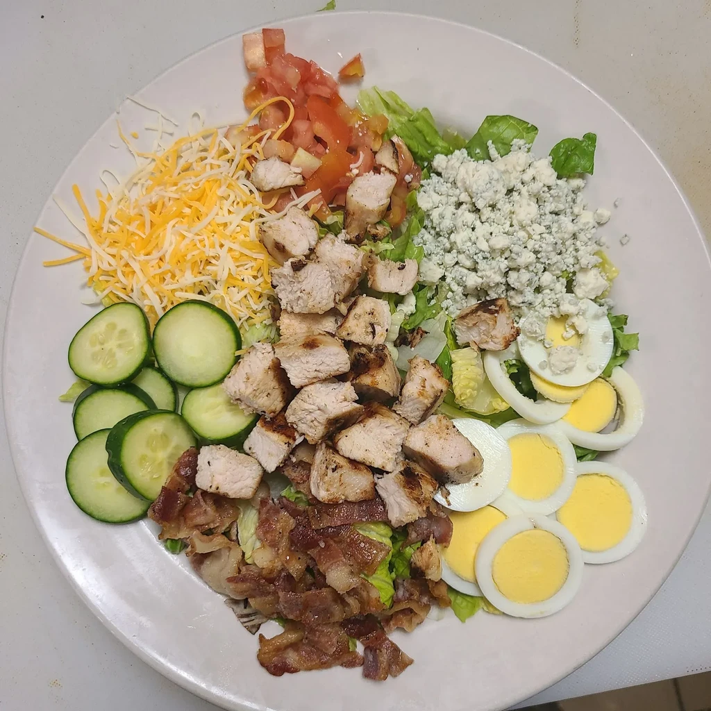 A vibrant Cobb-style salad with chicken, bacon, egg, cheese, and vegetables.