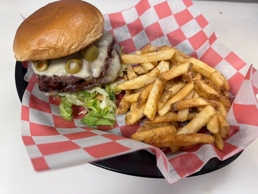 Burger with two patties, cheese, lettuce, olives, and golden fries.