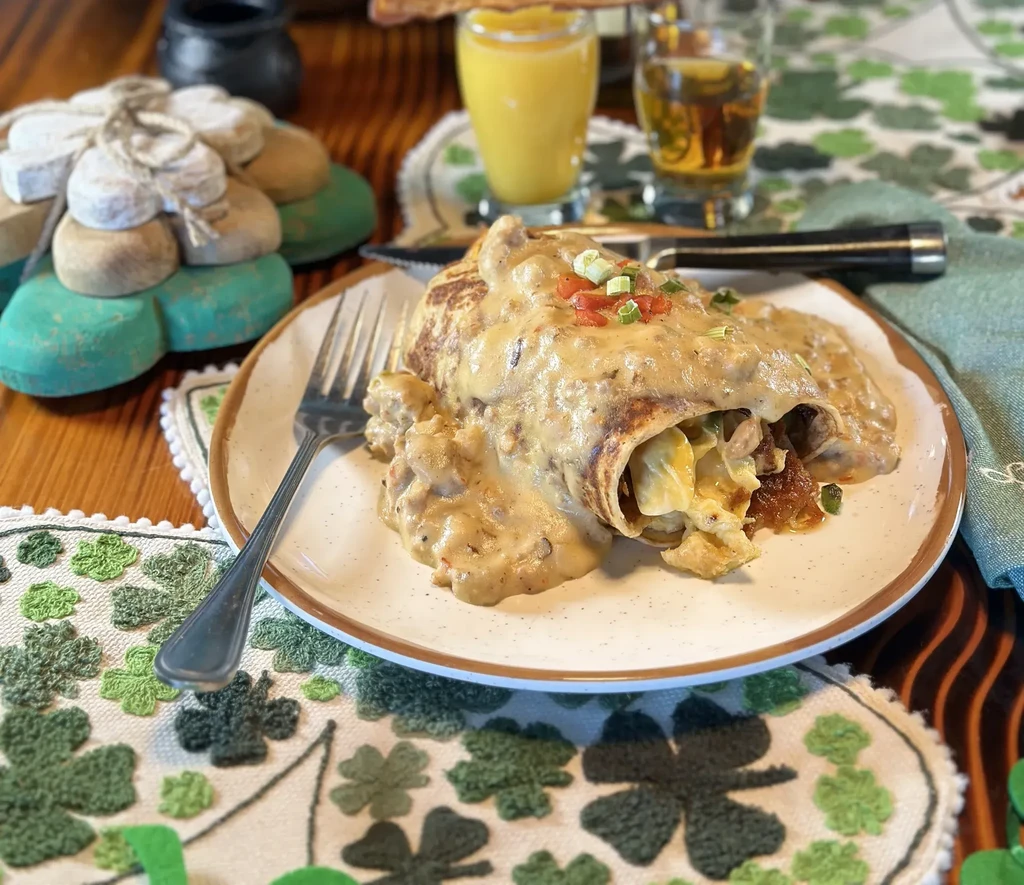 Gravy-covered breakfast burrito with eggs, tomatoes, and shamrock decor.