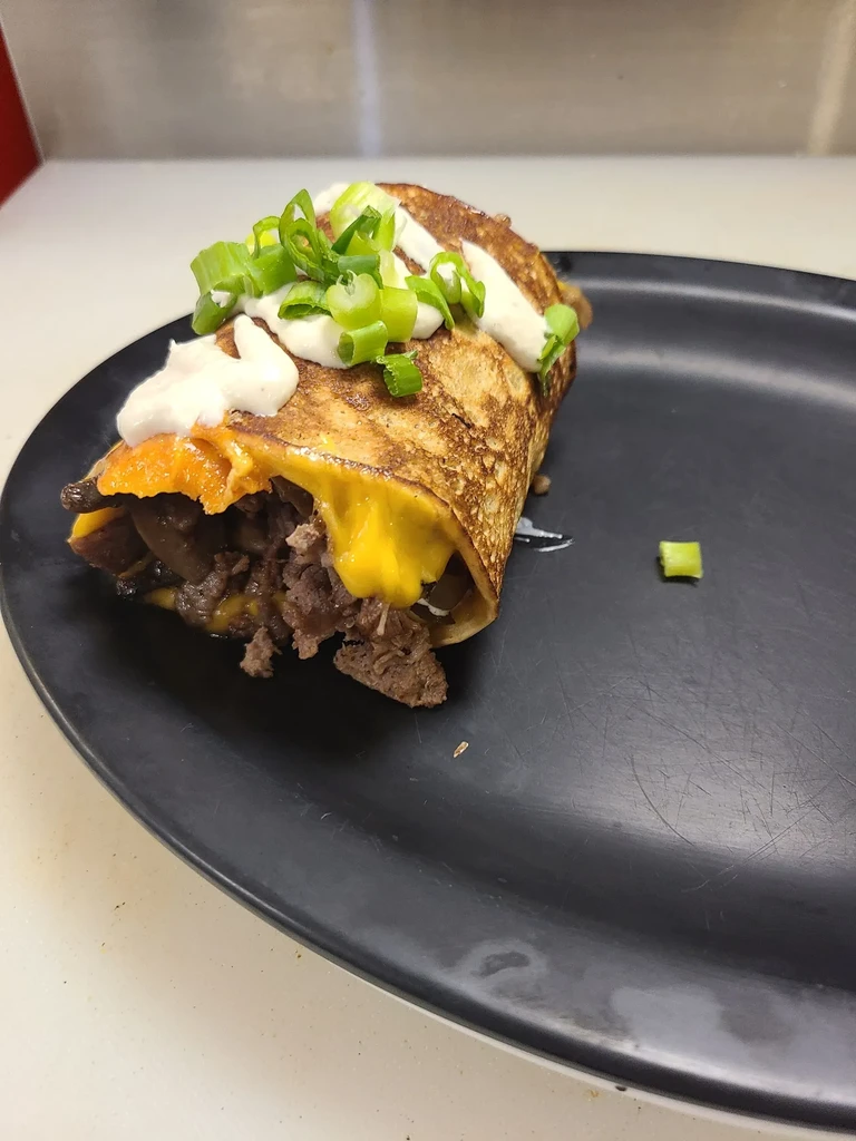 Savory meat and cheese wrap topped with creamy sauce and green onions.