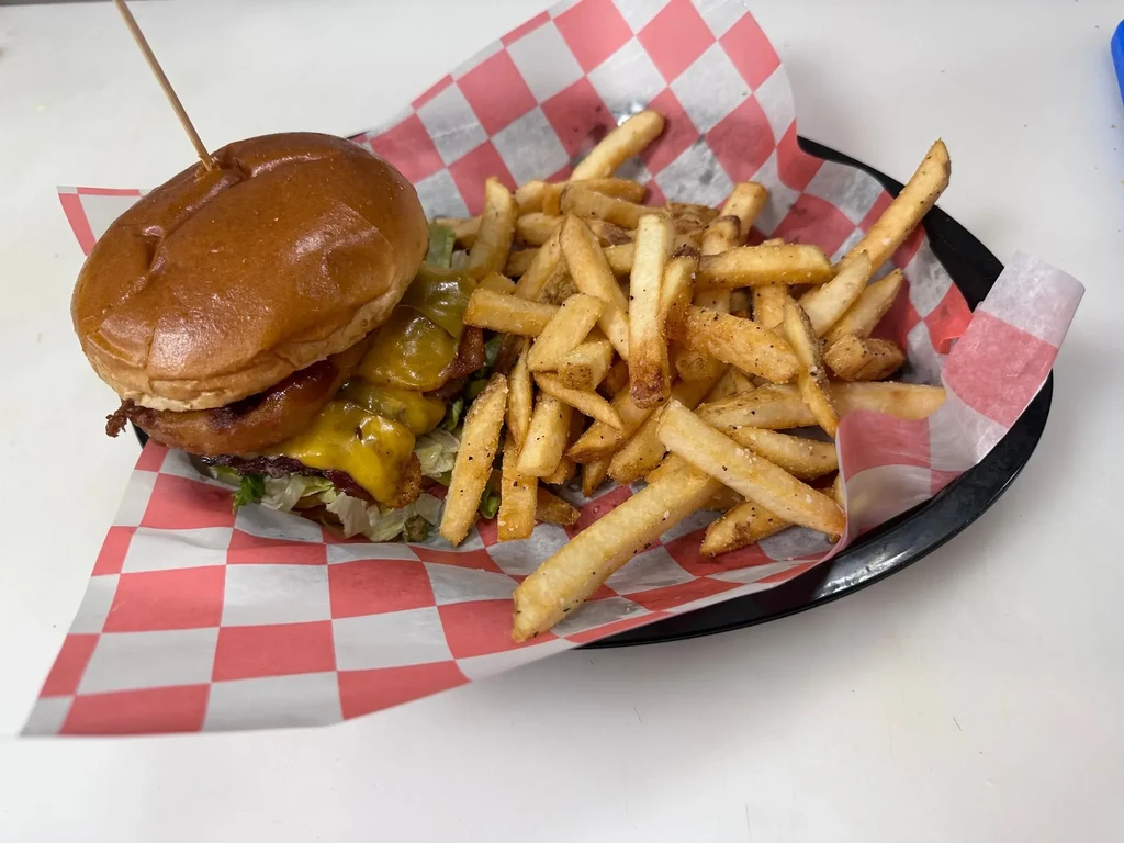 Close-up: Cheeseburger with toppings and seasoned fries in a black basket.