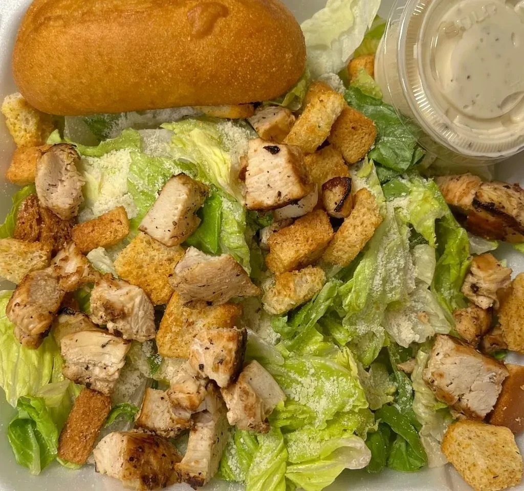 Grilled chicken Caesar salad with dressing, roll, in takeout container.
