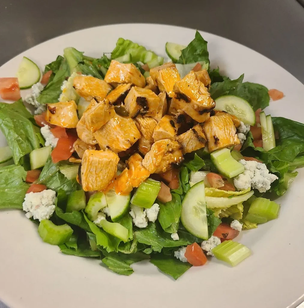 Close-up of grilled chicken salad with lettuce, tomato, cucumber, blue cheese.