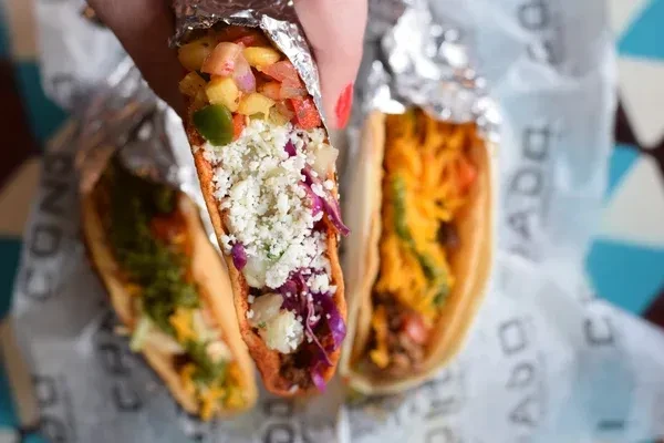 Three colorful tacos, one held, generously filled with fresh ingredients.