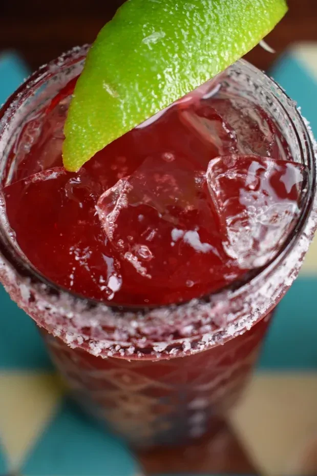 Bright red cocktail with ice, lime, and salted rim, top view.