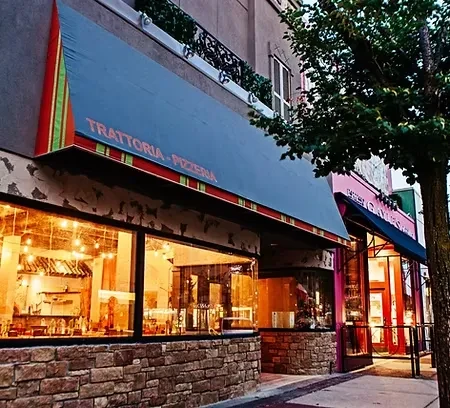 Warmly lit Trattoria Pizzeria with stone facade, pizza oven visible.