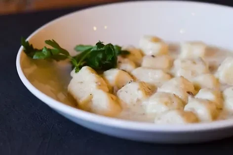 Potato dumplings with creamy sauce and parsley in a white bowl.