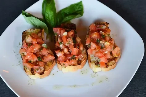 Three bruschetta with tomatoes, basil, and olive oil on a white plate.