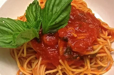 Spaghetti with chunky tomato sauce and fresh basil in a white bowl.