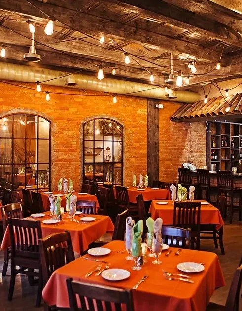 Empty restaurant interior with orange tables, brick walls, and Edison lights.