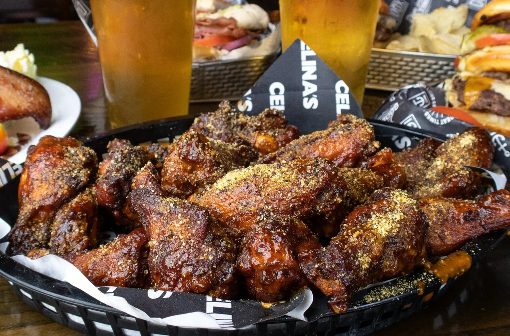 Black basket overflowing with glazed chicken wings and dry seasoning.
