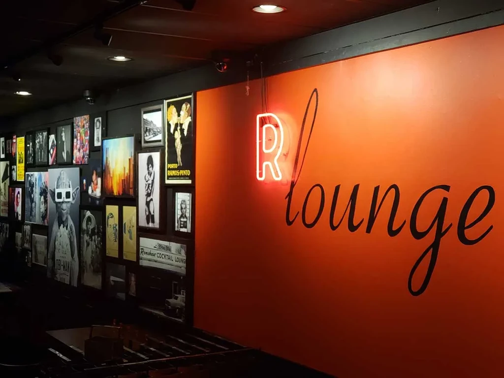 Dimly lit lounge with eclectic art wall and "R lounge" neon sign.