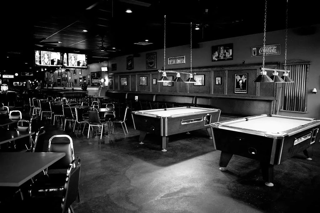 Black and white bar interior with two brightly lit pool tables.